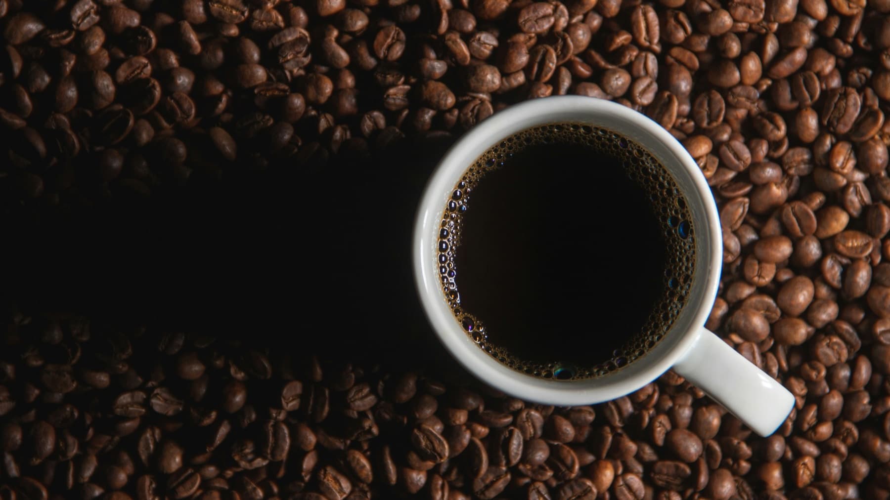 Taza de café oscuro rodeada de granos tostados
